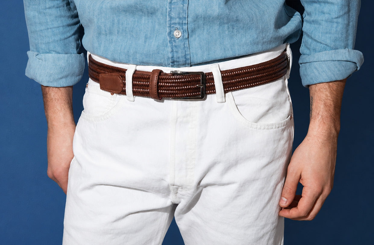 Person wearing a blue shirt, white pants, and a brown Beltology men's belt against a blue background