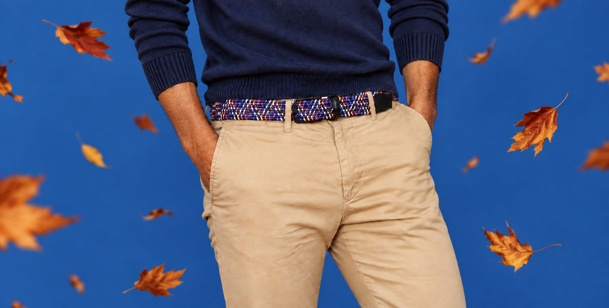 A person from the chest down wearing a navy sweater, beige pants, and a patterned woven mens belt
