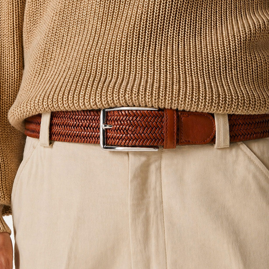 Brown woven mens belt with a silver buckle worn by a person in a beige sweater and pants