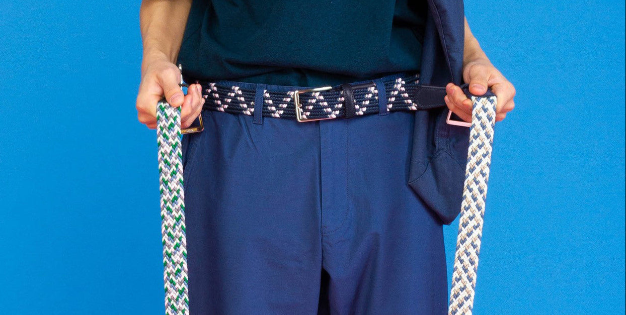 Model in blue clothing wearing a Beltology mens belt and holding a belt in each hand 