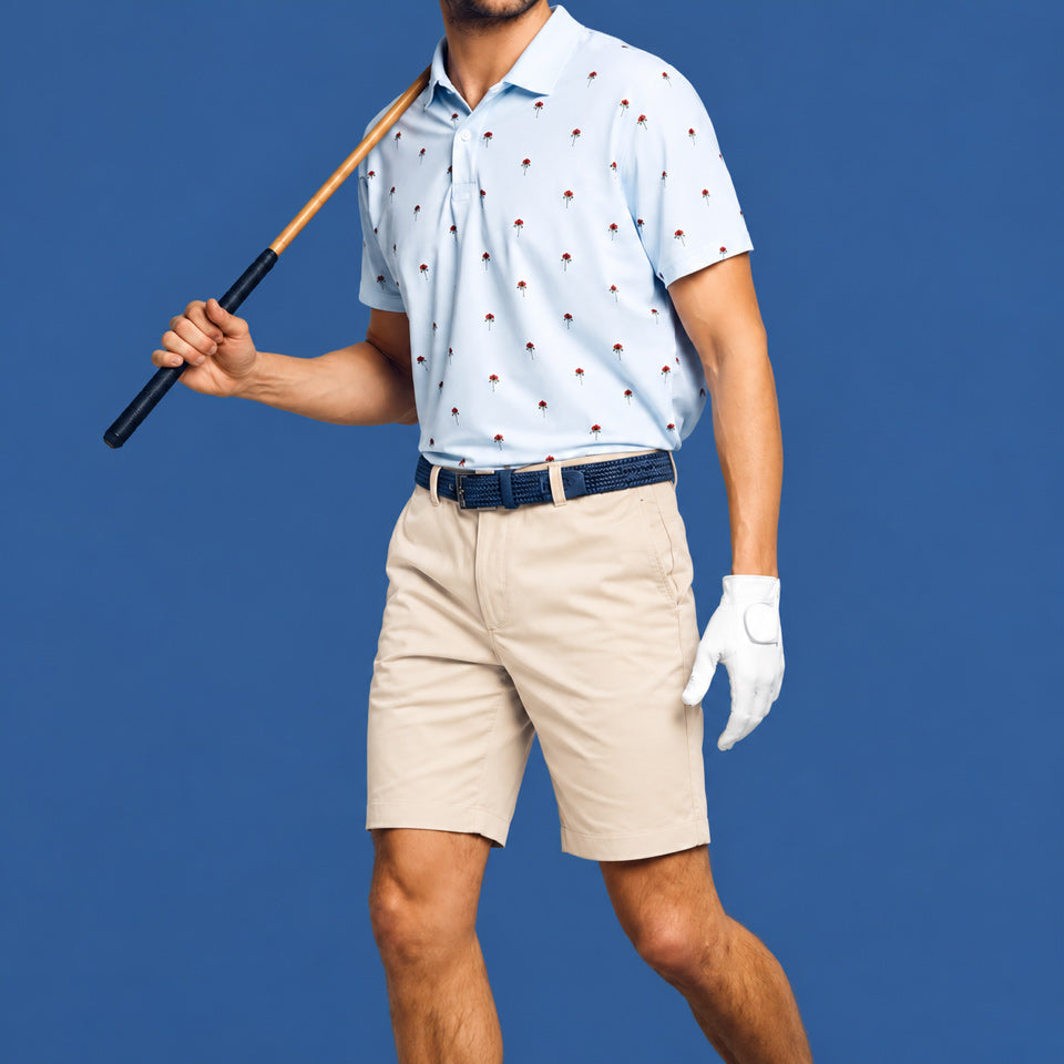 A man wearing a light blue short-sleeve polo shirt with a small red and gold golf ball pattern, khaki golf shorts, a dark blue men's belt, and a white golf glove, holding a golf club